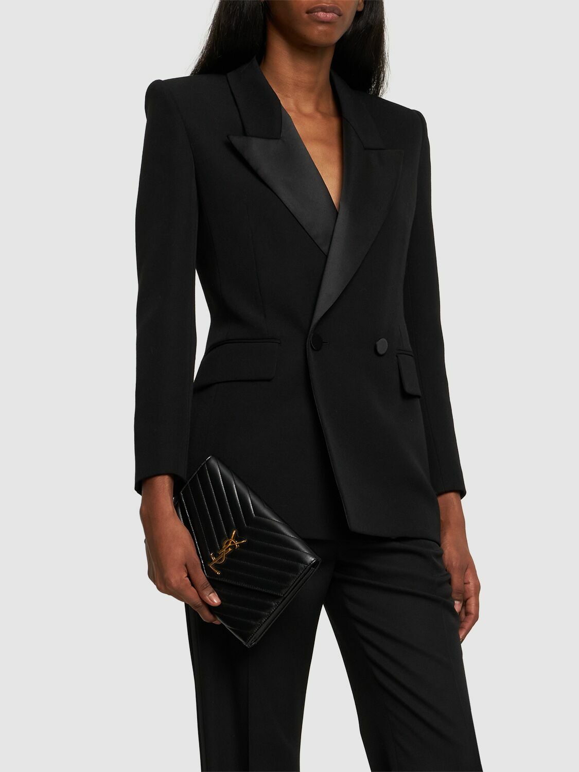 Model styling a black Saint Laurent Cassandre Clutch with sharp black tailoring.