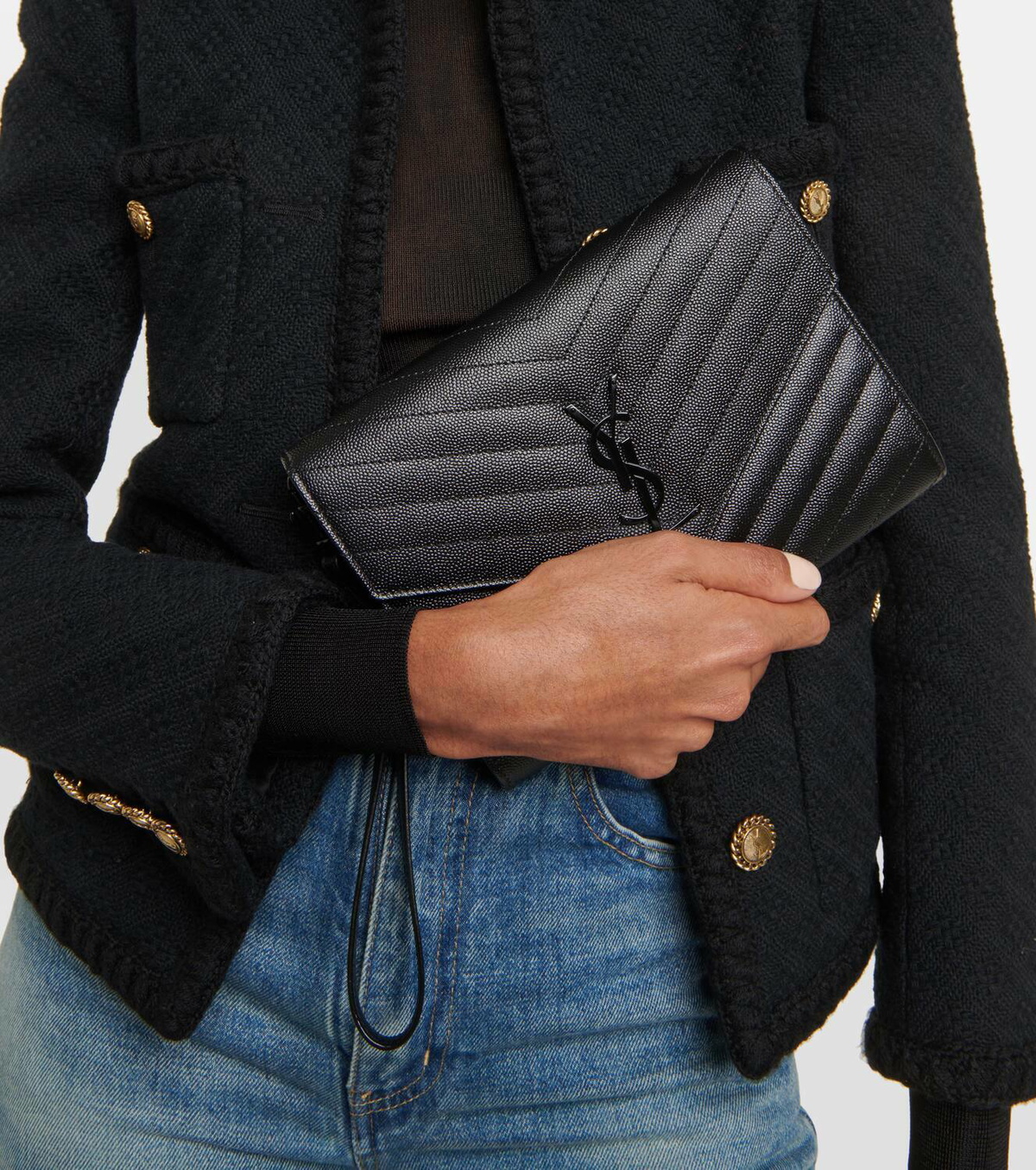Model carrying a black Saint Laurent Cassandre Clutch by its leather wristlet.